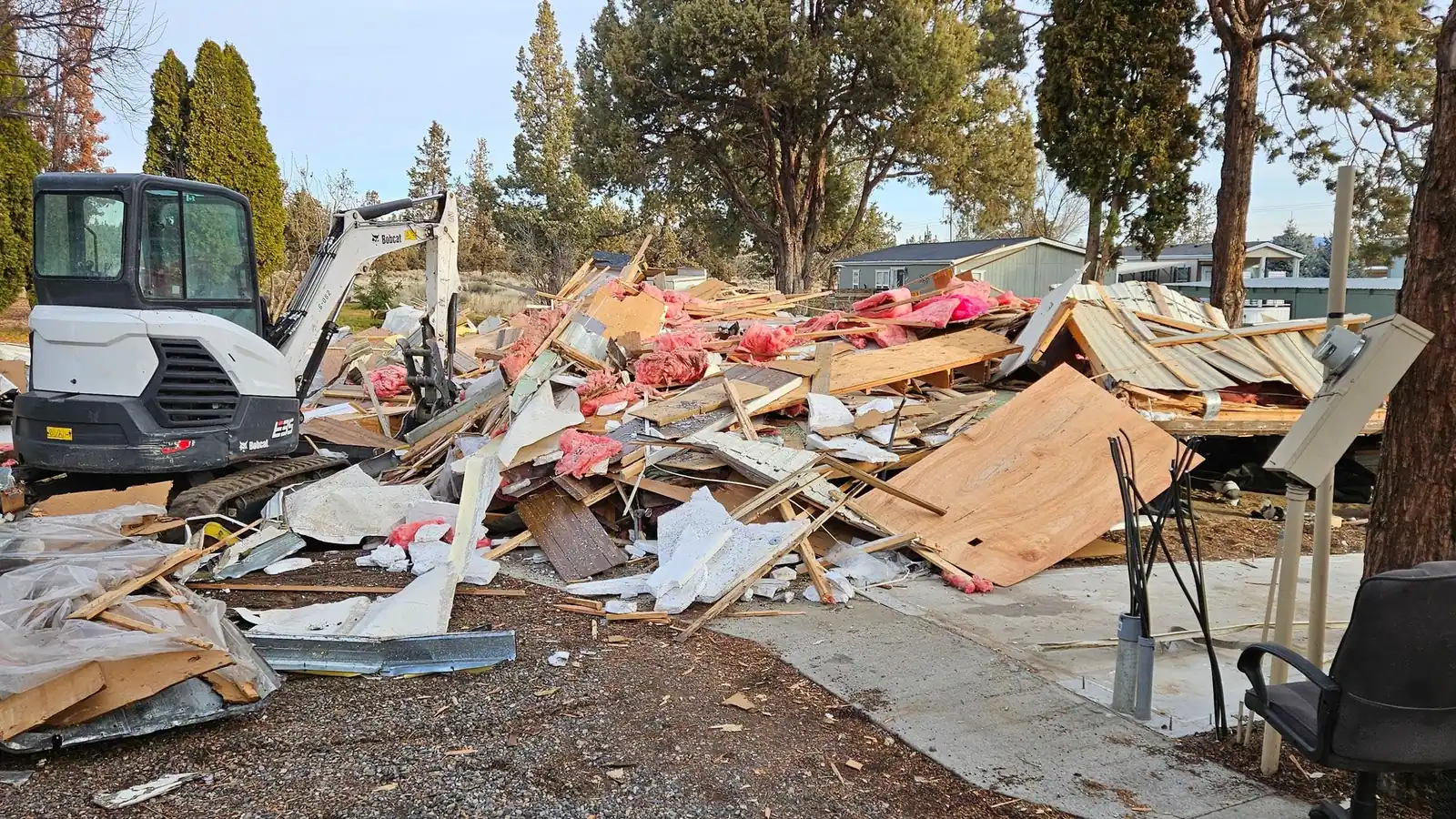 A large pile of demolition debris, siding and insulation next to a mini excavator