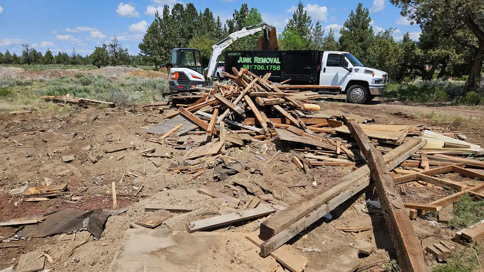 A pile of torn-down lumber with a mini excavator and the Superior Junk Removal truck behind it