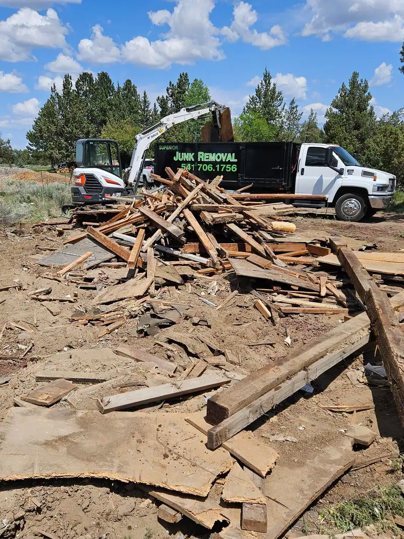 A pile of torn-down lumber with a mini excavator and the Superior Junk Removal truck behind it