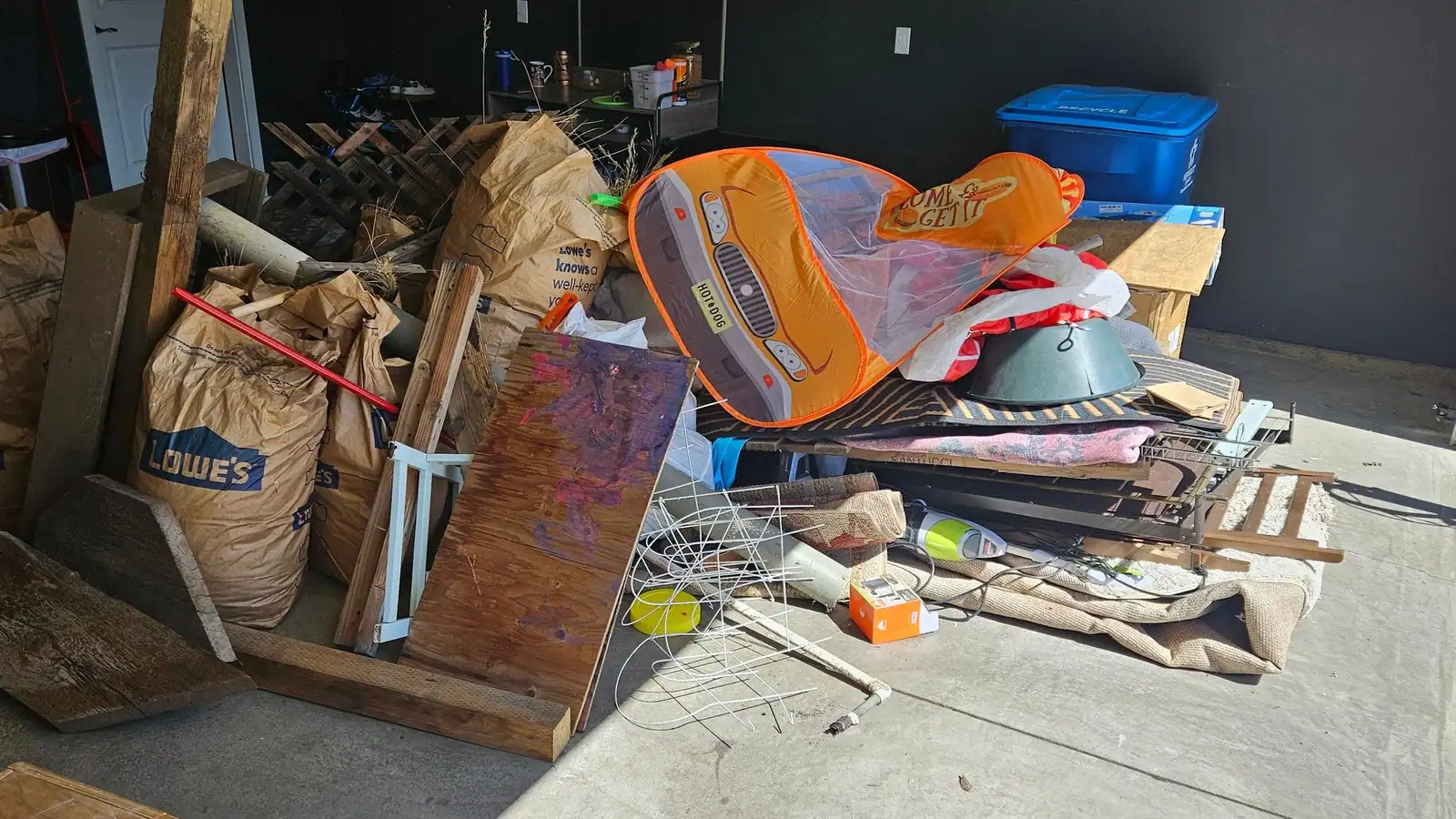A garage packed with old bins, a lawn chair, lumber and bags of junk