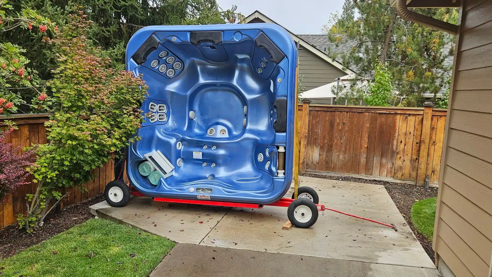A blue hot tub stood on its side on a red hot tub dolly