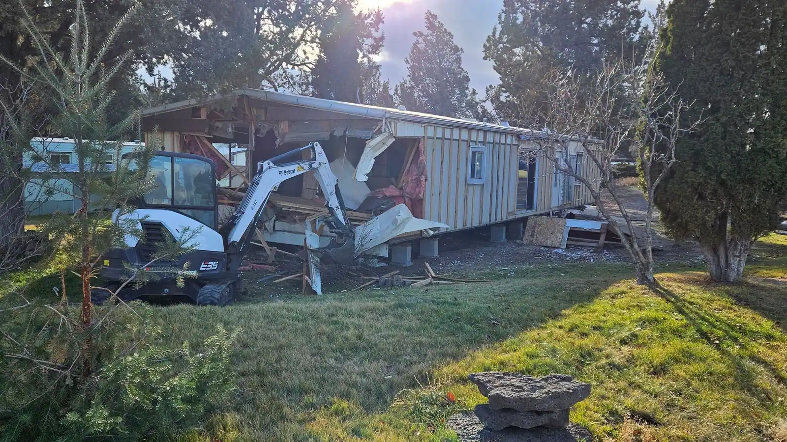 A mini excavator tearing down an old manufactured home