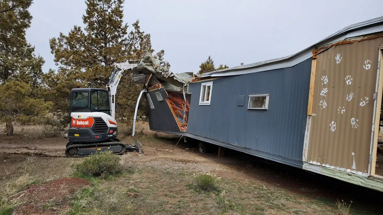 An excavator tearing down an old mobile home