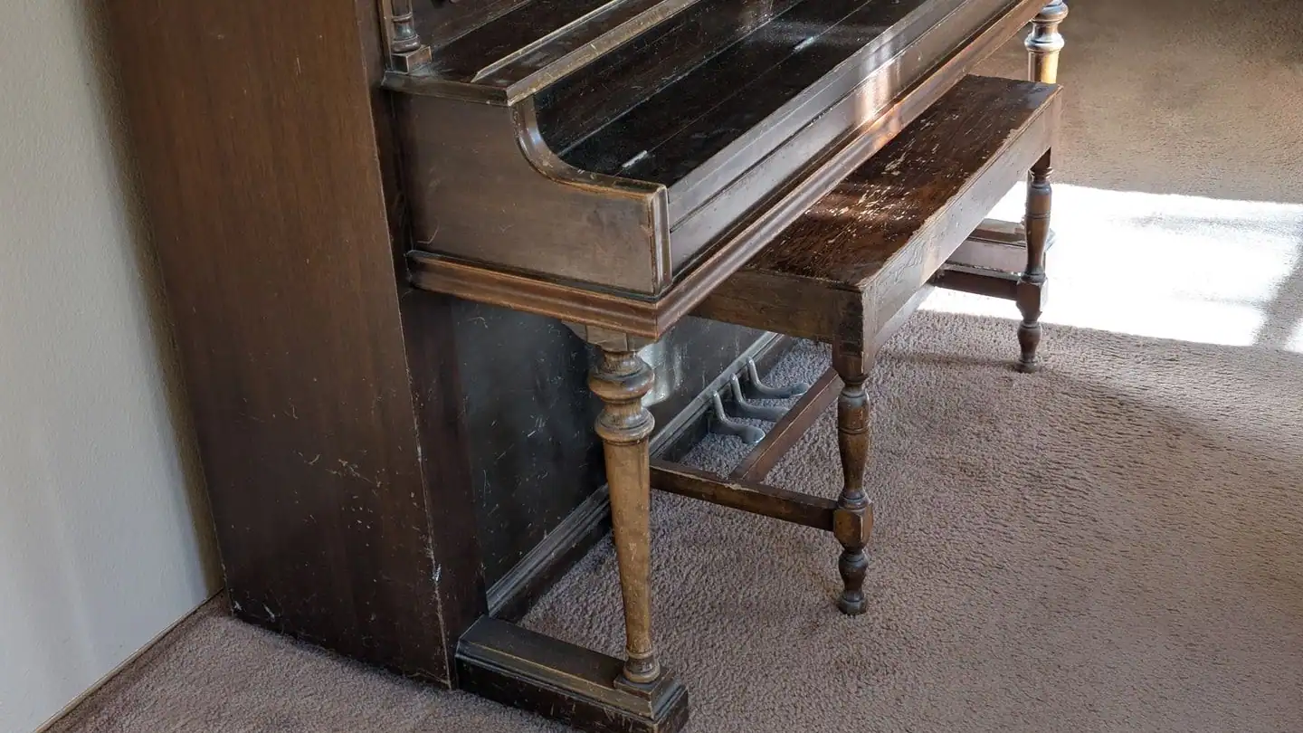 An old upright piano with its bench in a carpeted room