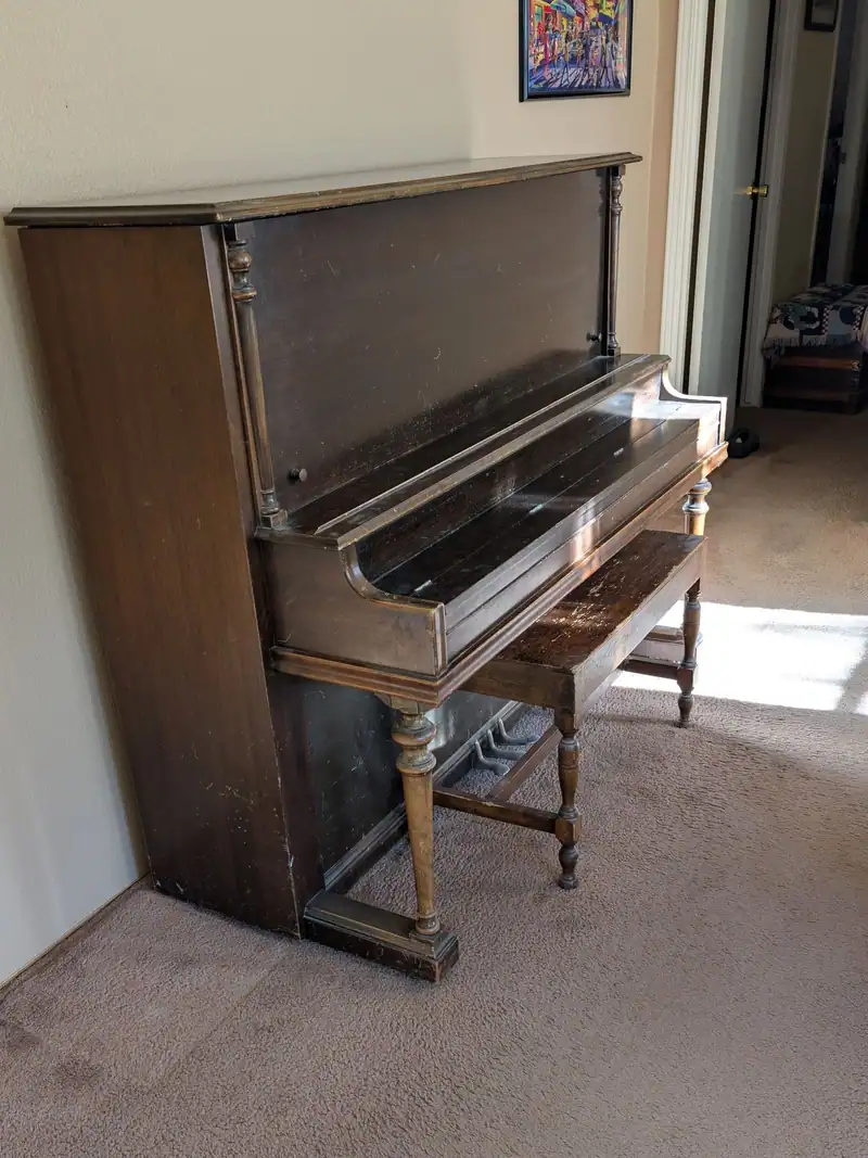 An old upright piano with its bench in a carpeted room
