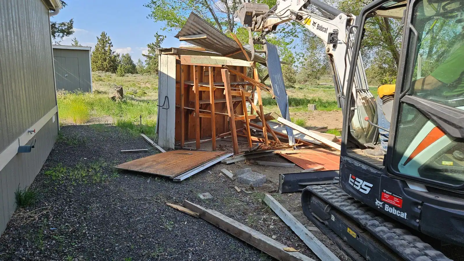 A mini excavator tearing down an old wooden shed