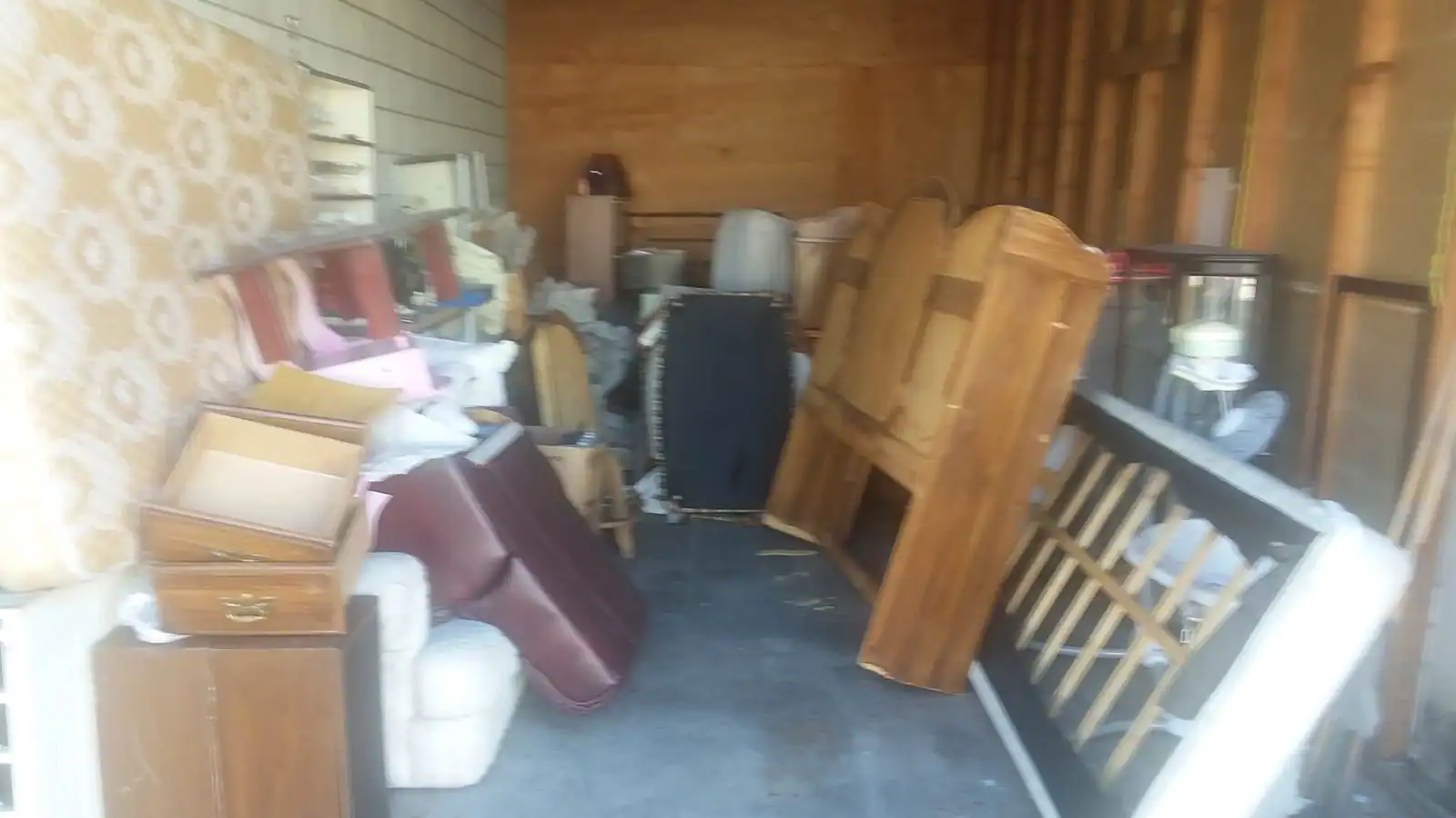 A storage unit full of old wood furniture, chairs and a cabinet