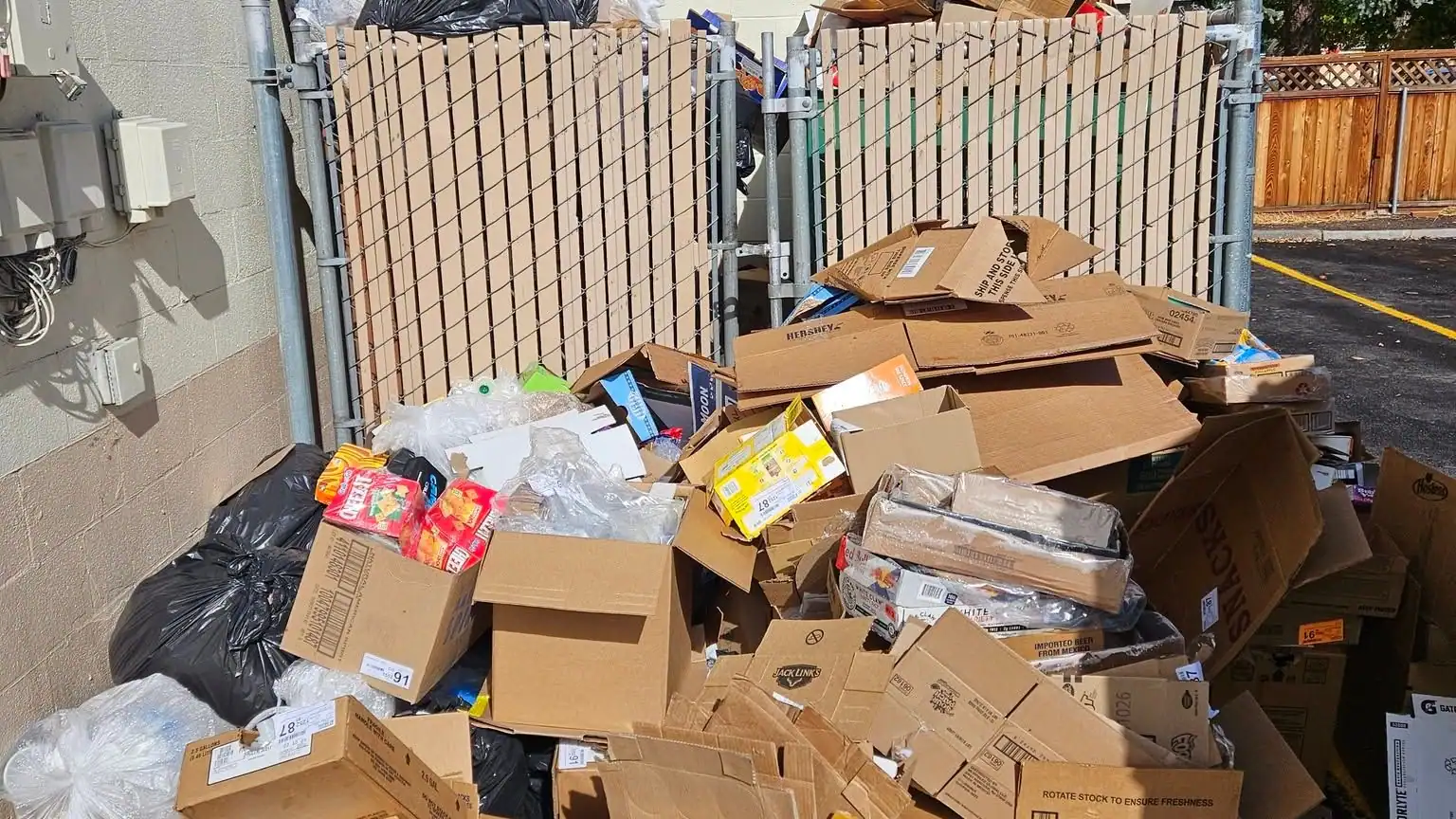 A pile of flattened boxes, bags and trash against a fence