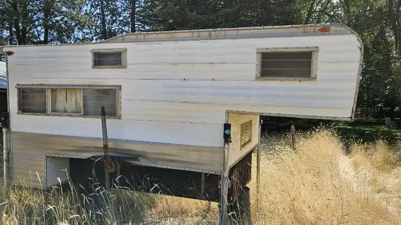 An old truck camper sitting in tall grass, ready to be torn down and hauled